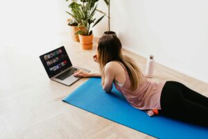 A young woman lying on a yoga mat, browsing on her laptop, enjoying leisure time indoors.