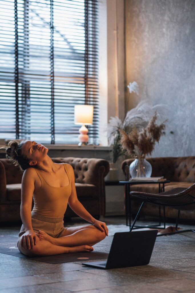 A woman practicing yoga indoors, utilizing a laptop for guidance. Calm atmosphere with tranquil decor.